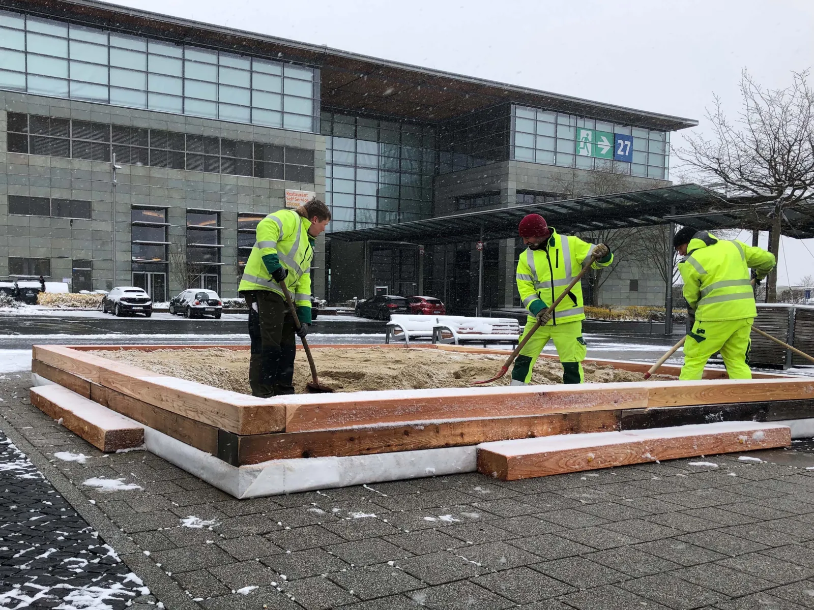 Drei Personen, die bei Schnee einen Sandkasten herrichten.